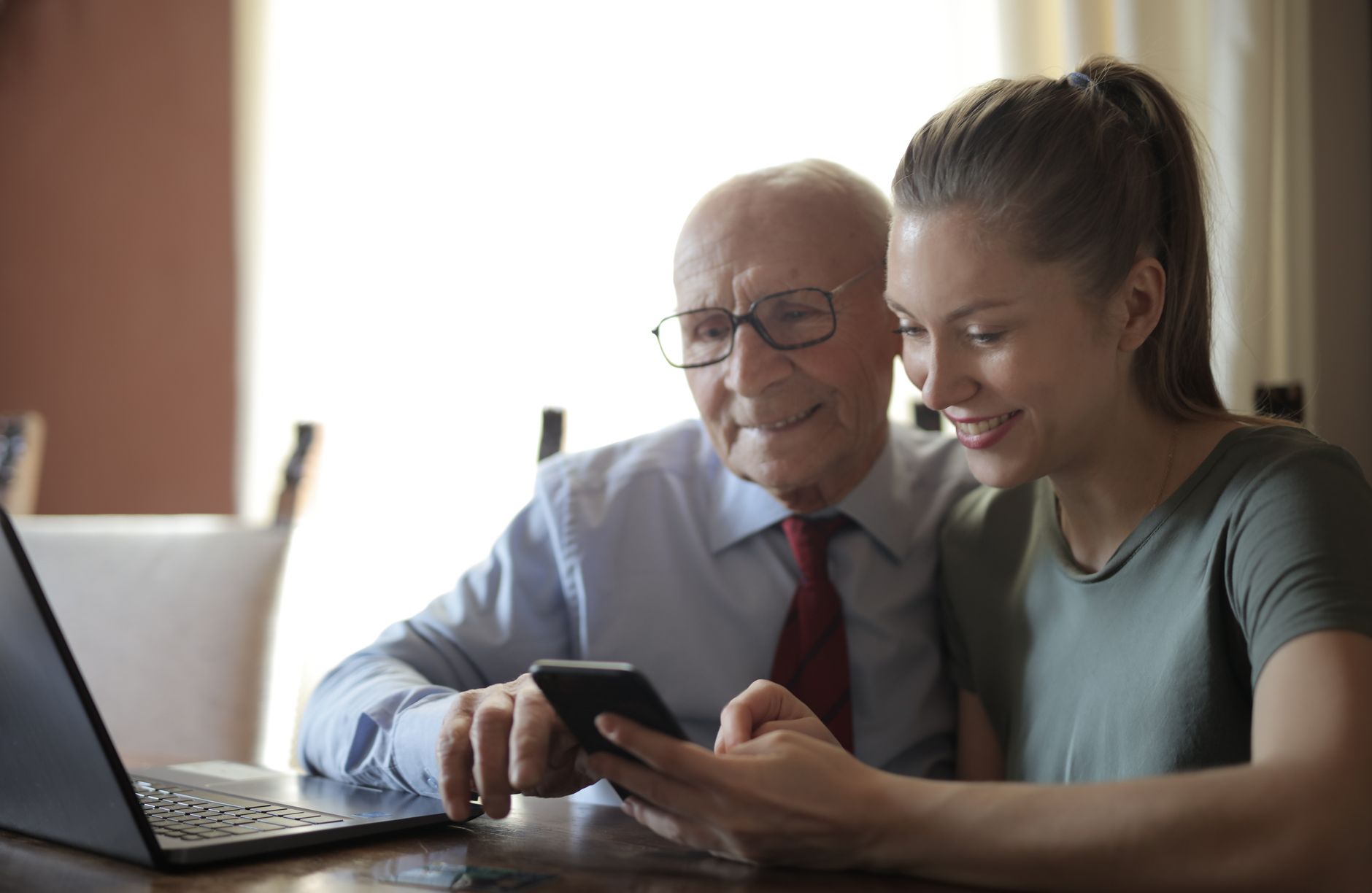 Un senior et une jeune femme consultent ensemble un smartphone devant un ordinateur portable.