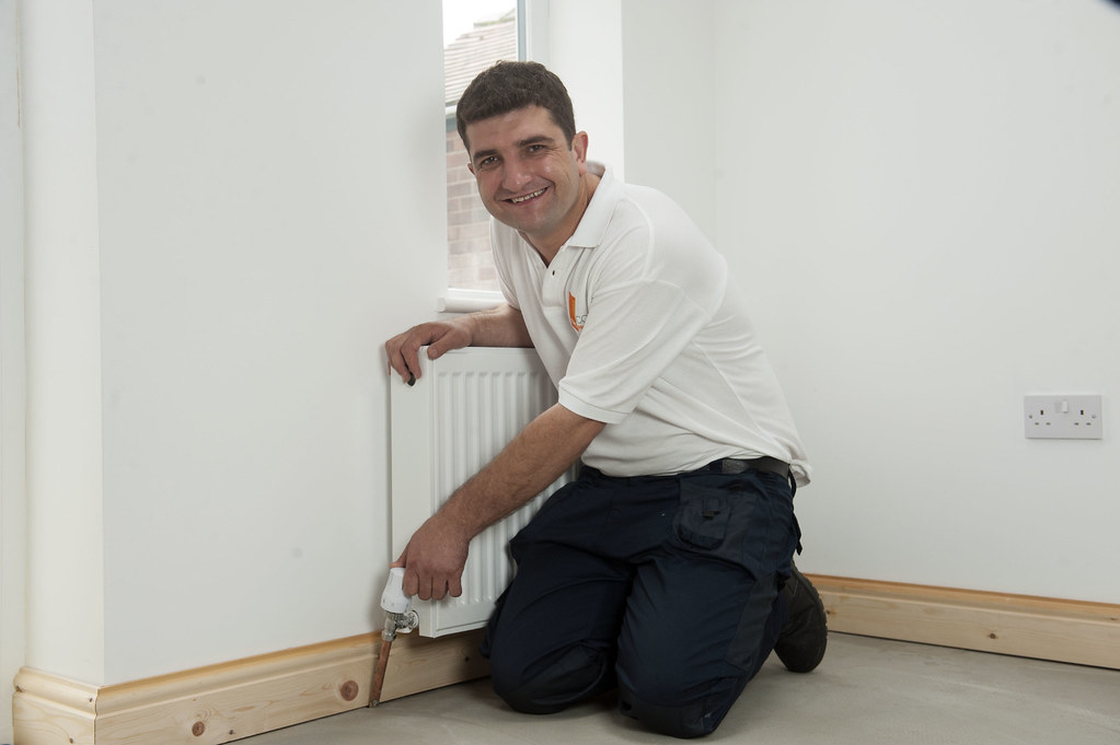 Chauffagiste agenouillé devant un radiateur de chauffage central pendant une intervention à domicile.