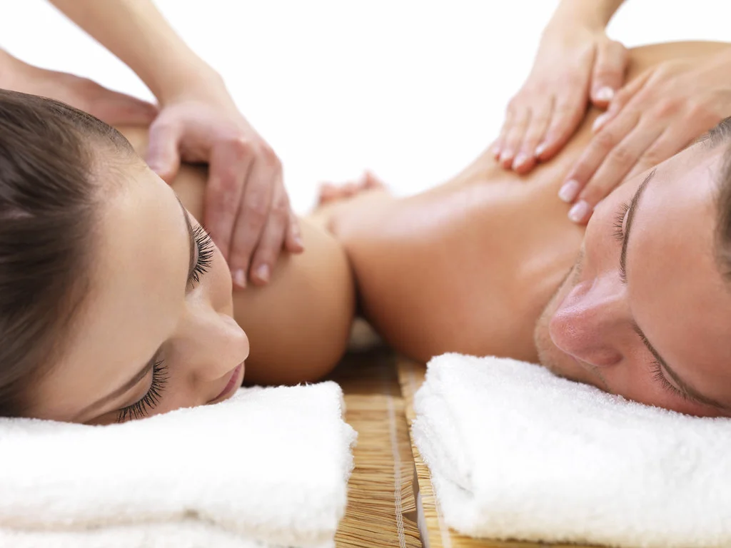 Couple allongé recevant un massage du dos en duo dans un spa, serviettes blanches et table en bambou