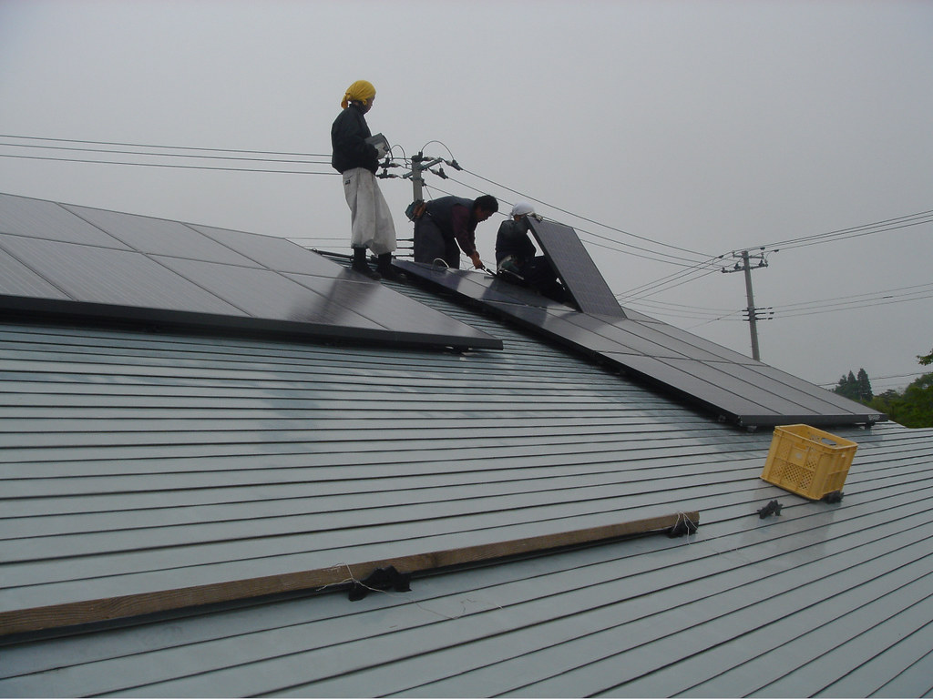 Techniciens posant des panneaux solaires photovoltaïques sur la toiture métallique d'une maison.