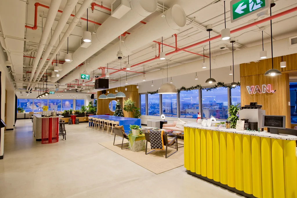 Grand espace de coworking lumineux avec lounge, bar et postes de travail partagés.