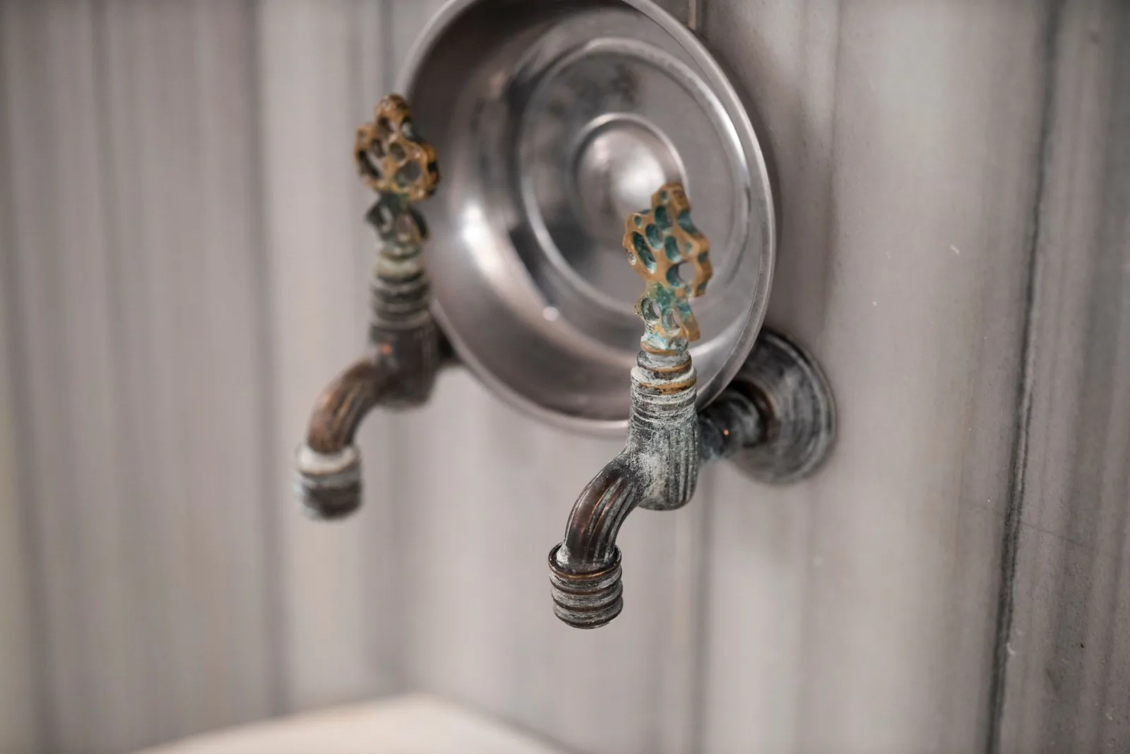 Robinets en laiton patiné au-dessus d'une vasque en métal, dans un hammam traditionnel en marbre.