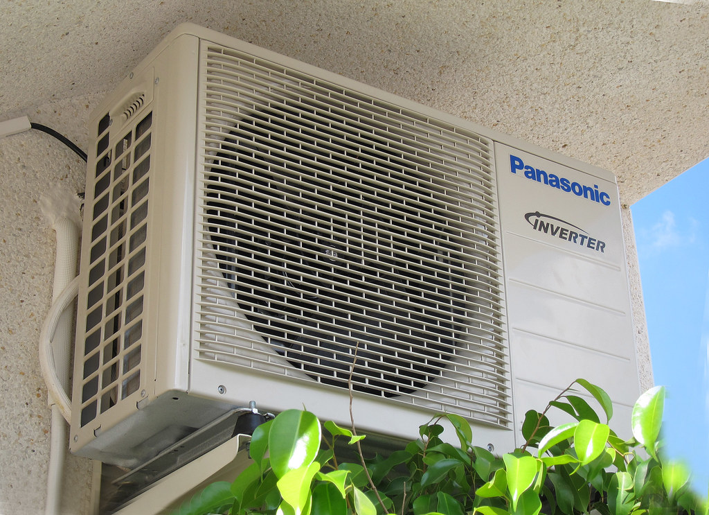 Unité extérieure de climatisation fixée sur une façade, avec grille de ventilation visible.